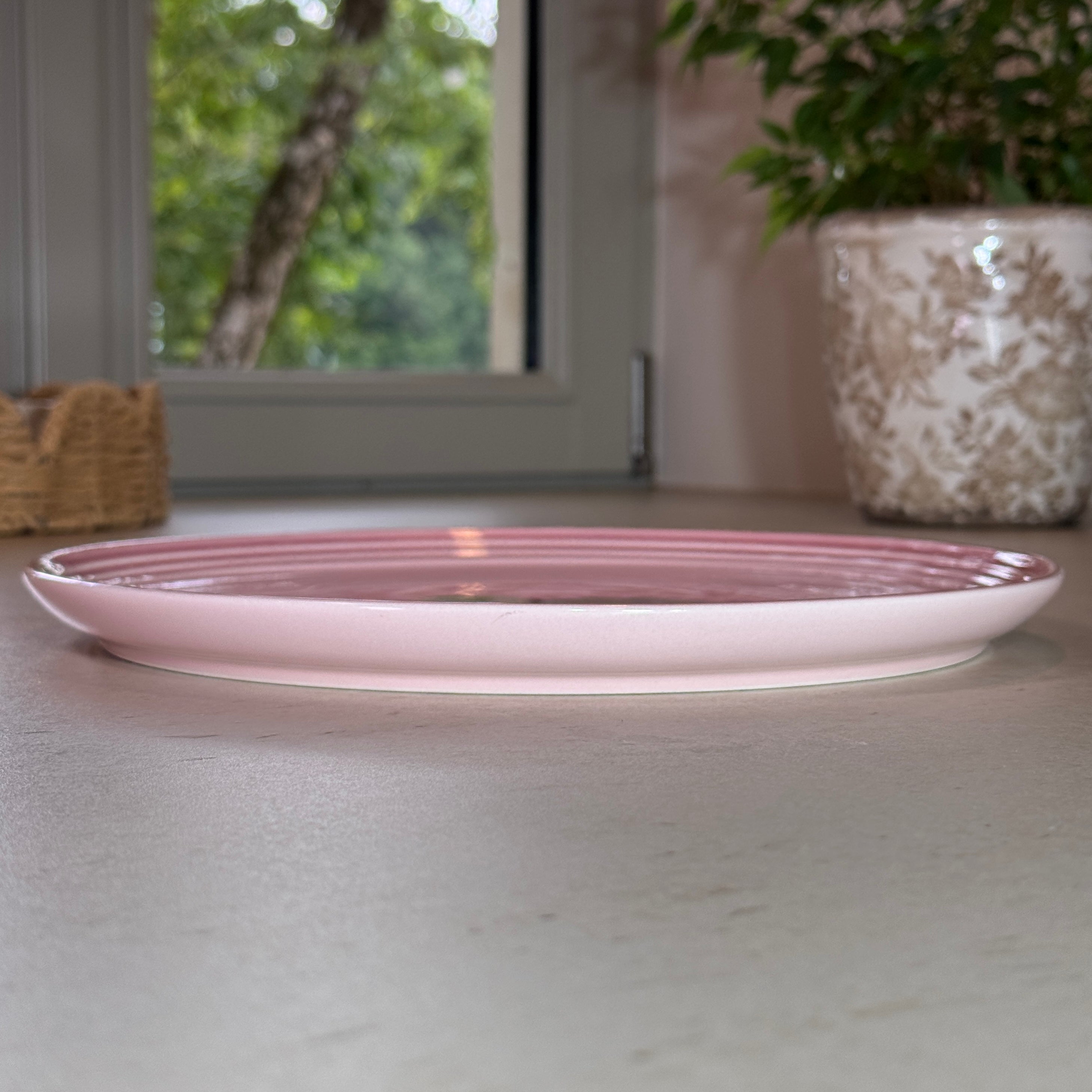 Vue de profil des assiettes en céramique émaillée rose avec finition brillante et rebord légèrement relevé.